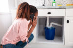 woman on phone looking at leak under sink