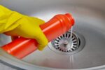 Gloved hand pouring drain cleaner in sink
